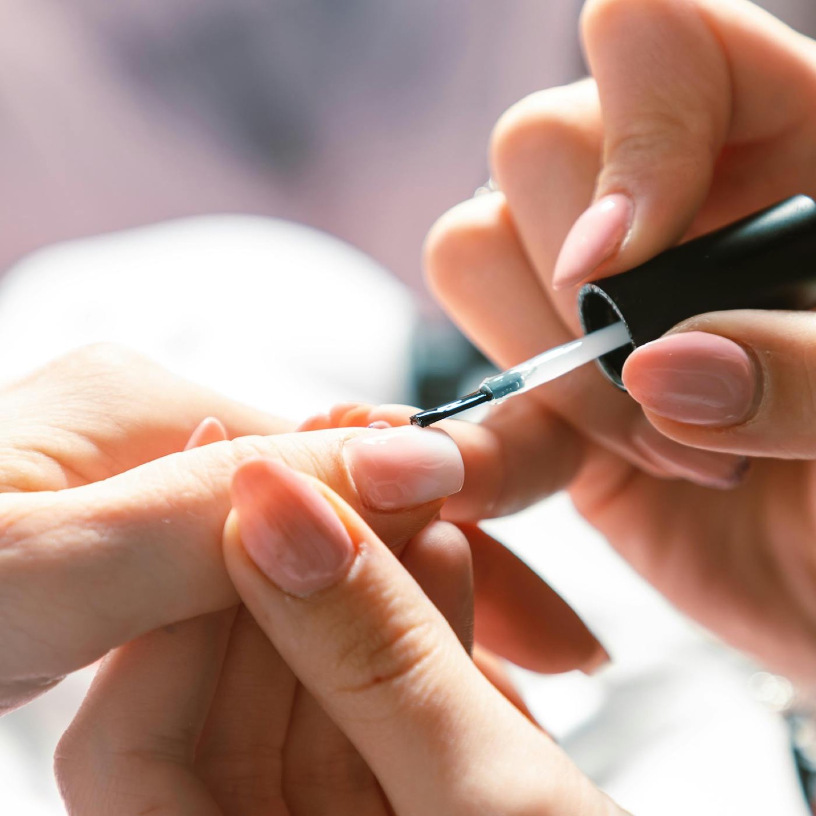 Technician applying soft pink polish to a client's fingernail