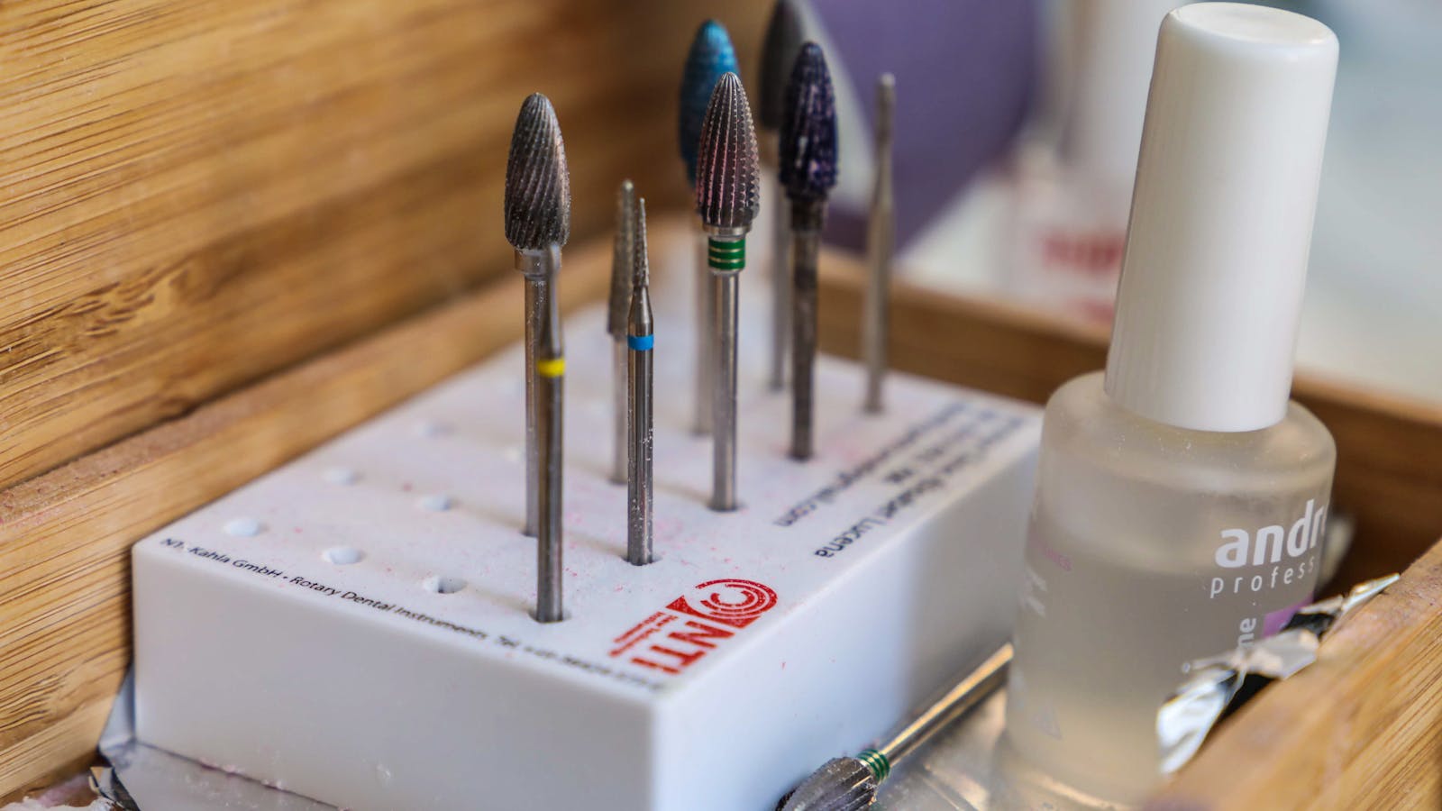 Nail drill bits and a matte top coat bottle arranged in a wooden tray