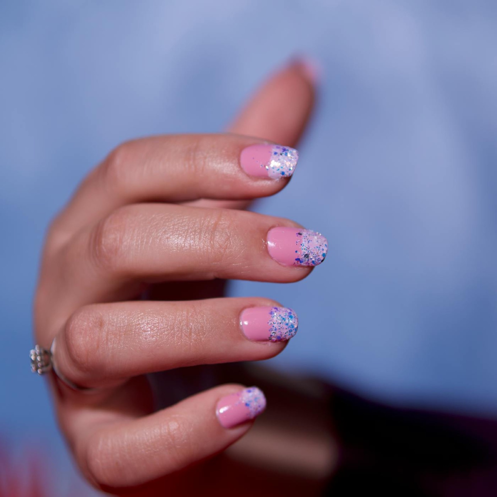 Short pink French manicure with glitter tips against a blue background